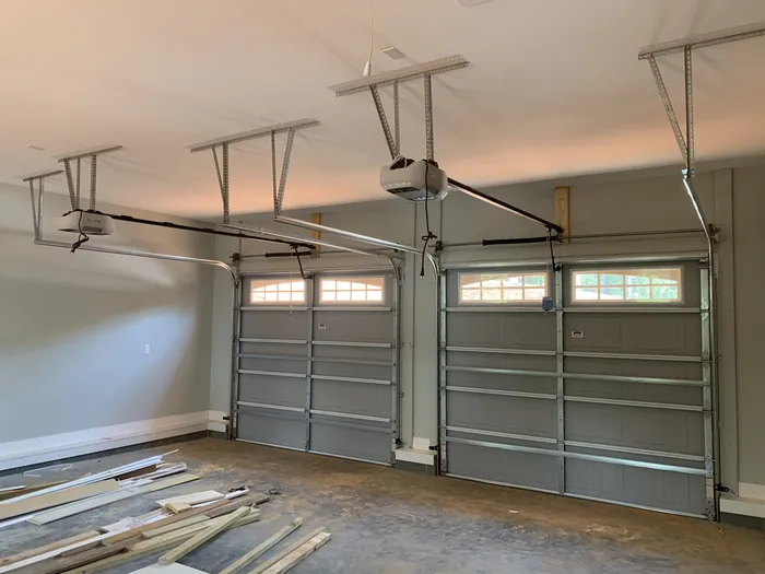 Interior of a double garage with two sectional doors on ceiling mounted openers, rails and torsion springs visible
