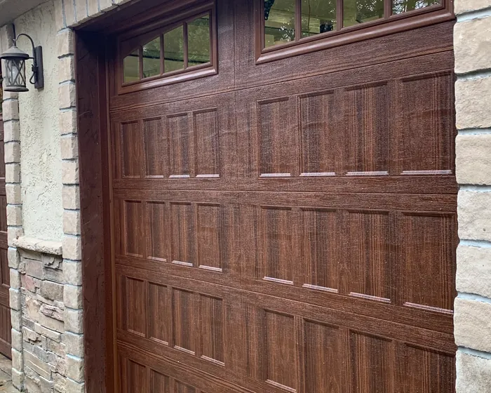 Two dark walnut woodgrain carriage house garage doors with arched window sections in a stone and stucco surround