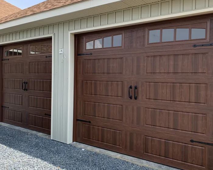 Two dark walnut woodgrain garage doors with black handles and strap hinges on a cream board and batten elevation