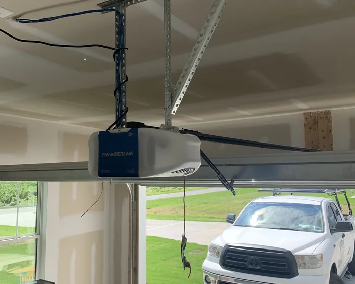 A Chamberlain garage door opener mounted to the ceiling on cut angle iron above an open garage door